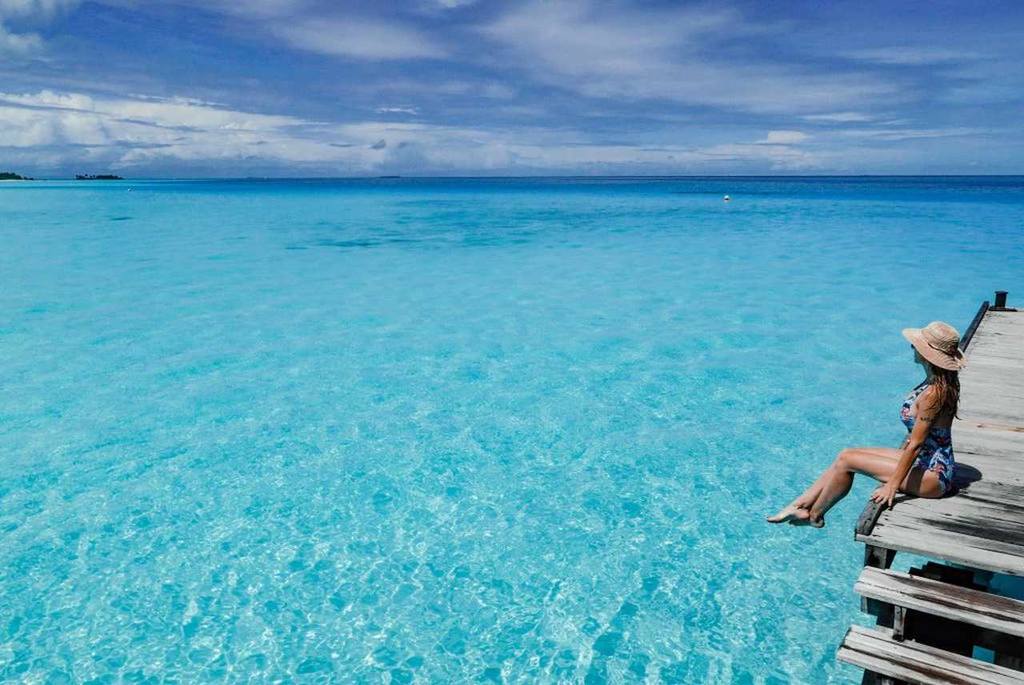 Oceano cristalino com pessoa sentada sobre a beira domarOnde fica as Maldivas Brasileira